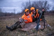 Two hunters sit behind a freshly-harvested deer. 