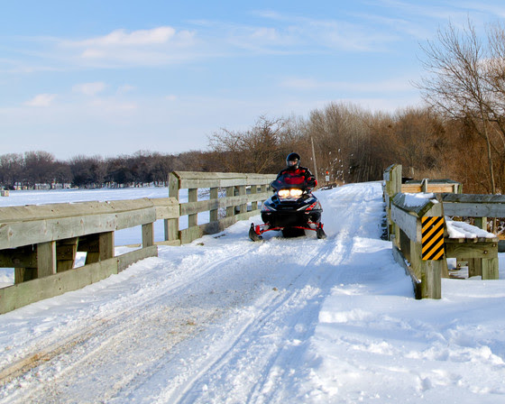 A snowmobiler crosses a snow covered bridge