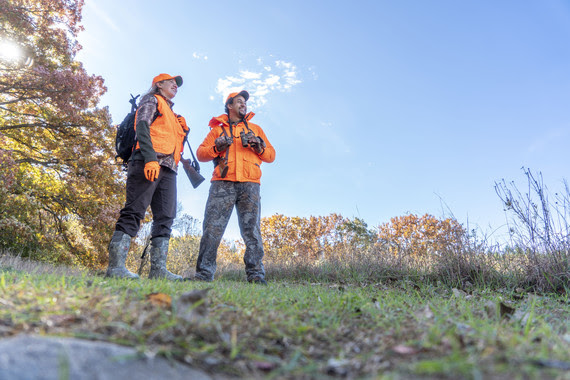 Two hunters stand together while out in the field. 