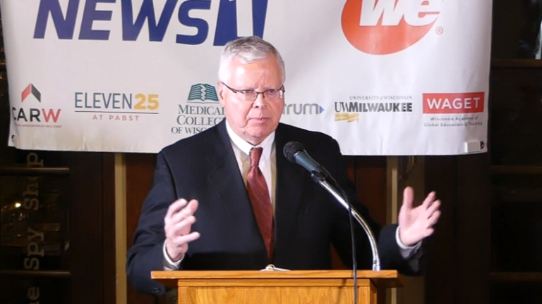 This image shows Universities of Wisconsin President Jay Rothman speaking at a podium at a WisPolitics-Milwaukee Press Club event.