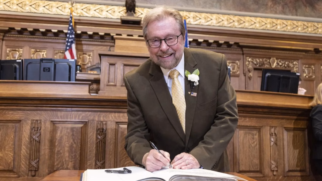 Picture of Rep. Rick Gundrum in the Assembly Chamber posing while signing a large book.