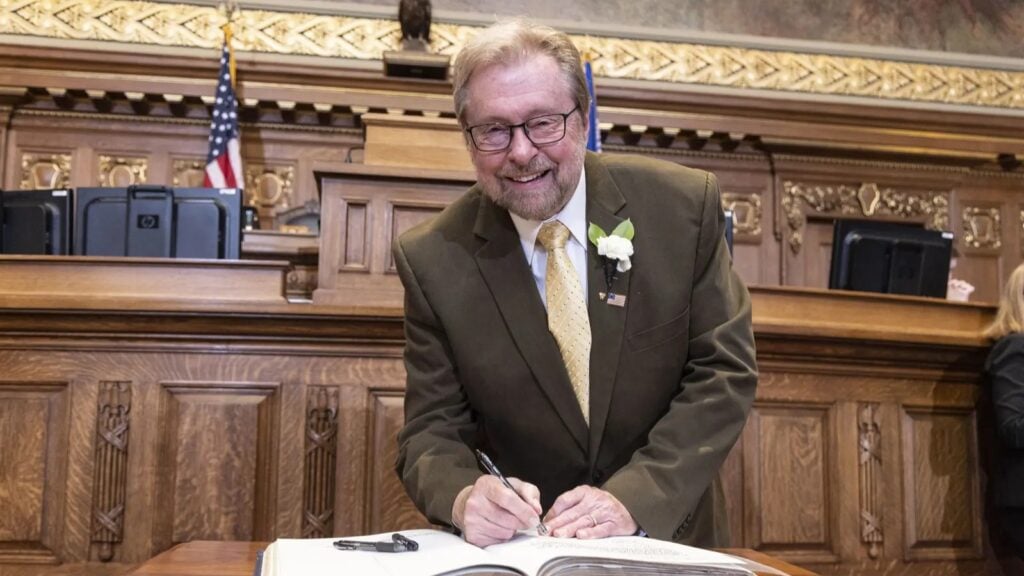 Picture of Rep. Rick Gundrum in the Assembly Chamber posing while signing a large book.