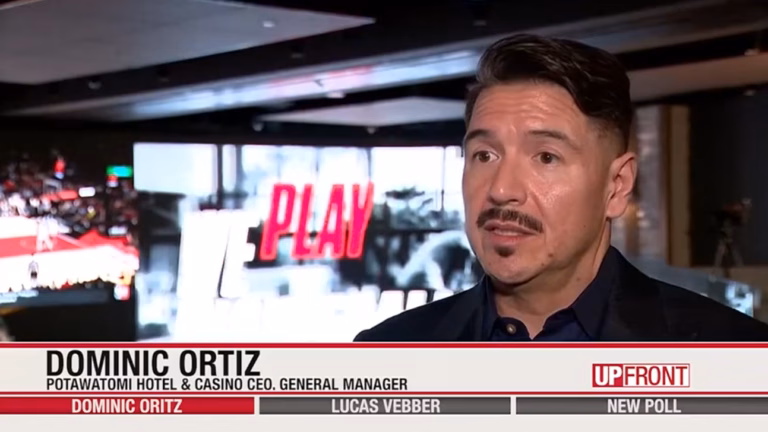 Photo of Potawatomi Casino & Hotel CEO Dominic Ortiz standing in front of a large LCD screen with the word "play" dispalyed on it.