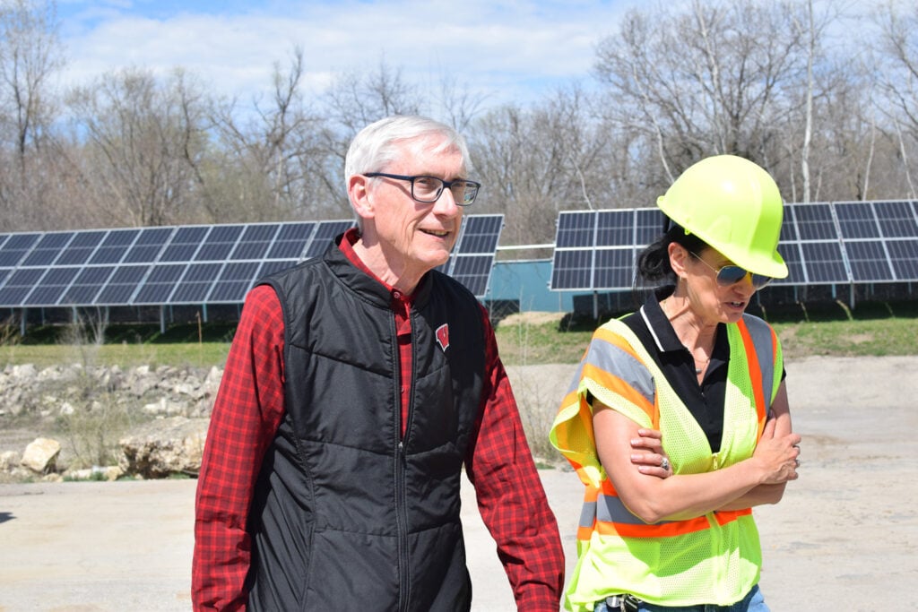 Gov. Tony Evers wals with a worker in front of ground-mounted solar cells.