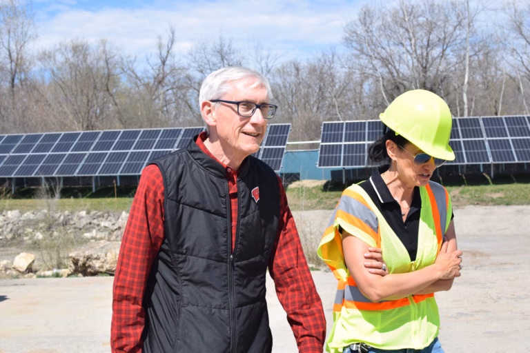Gov. Tony Evers wals with a worker in front of ground-mounted solar cells.